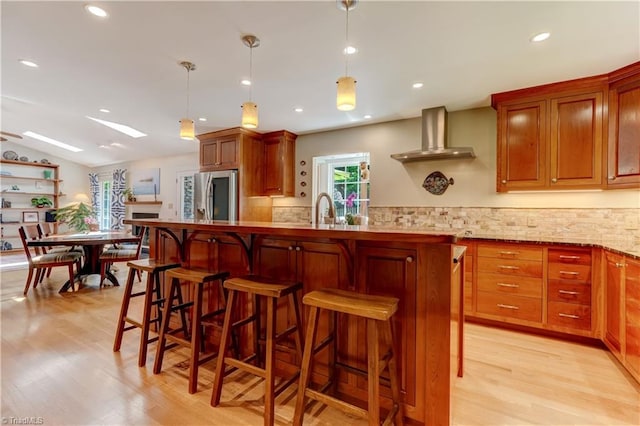 7 Pineburr Ct, Greensboro, NC 27455 - kitchen featuring stainless steel fridge, wall chimney range hood, light wood-style floors, tasteful backsplash, and a breakfast bar