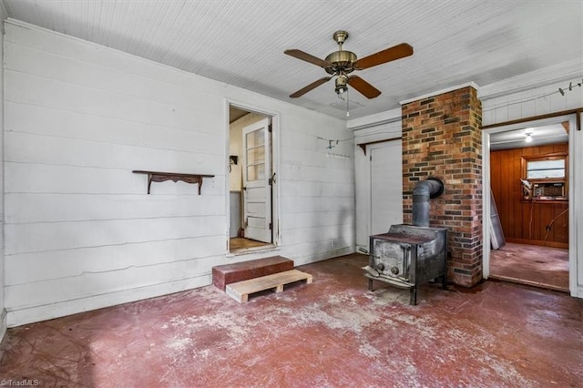 living room with concrete floors, a ceiling fan, a wood stove, and wooden walls