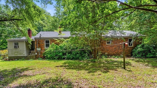 back of house featuring a chimney, a yard, and brick siding