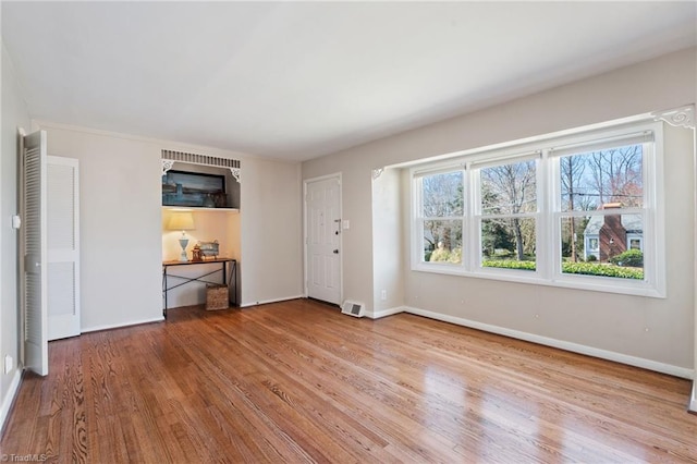 unfurnished living room with wood finished floors, visible vents, and baseboards