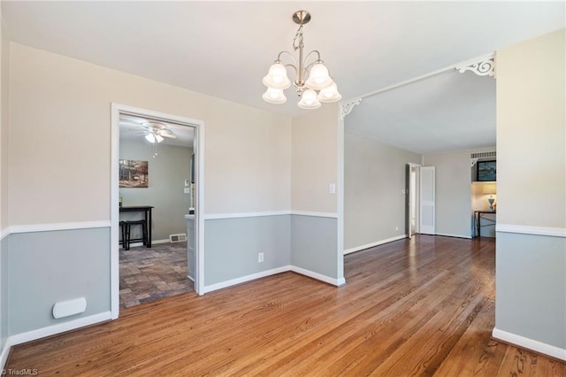 empty room featuring visible vents, baseboards, a notable chandelier, and wood finished floors