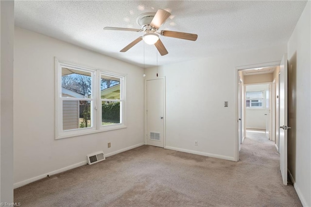 carpeted empty room with visible vents, plenty of natural light, a textured ceiling, and baseboards