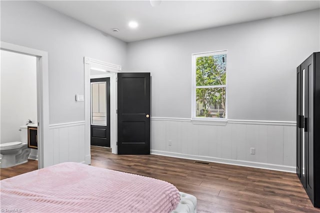 bedroom with baseboards, connected bathroom, wainscoting, and dark wood-style floors