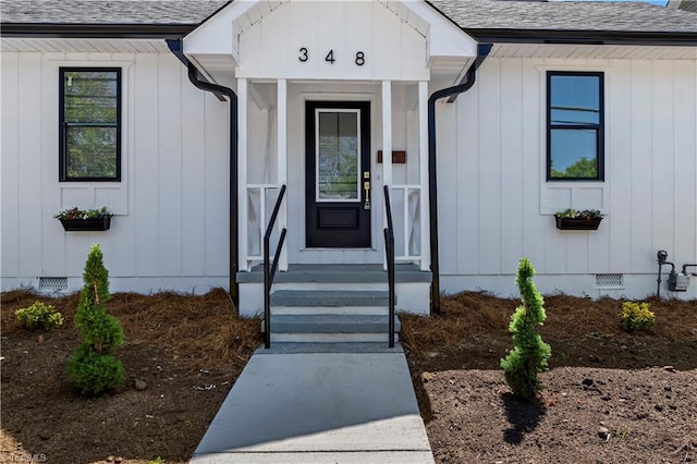 view of exterior entry with board and batten siding, crawl space, and roof with shingles