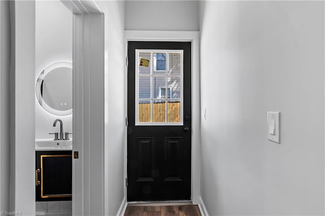 doorway featuring baseboards, a sink, and wood finished floors