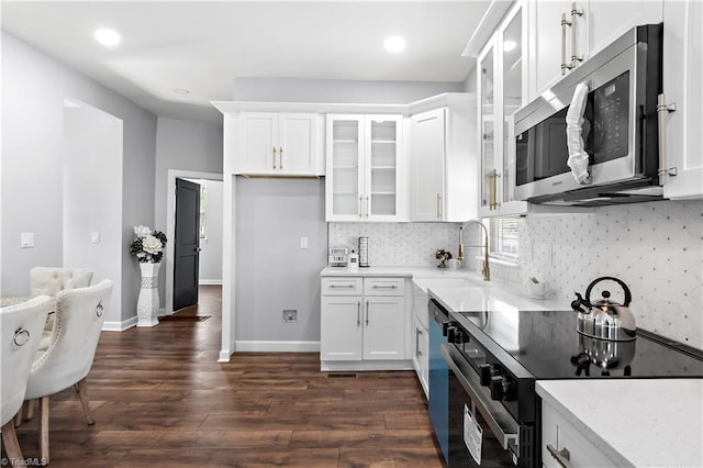 kitchen with white cabinets, dark wood-style flooring, appliances with stainless steel finishes, a sink, and glass insert cabinets