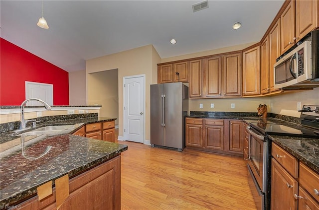 kitchen with stainless steel appliances, decorative light fixtures, light wood-type flooring, dark stone counters, and sink