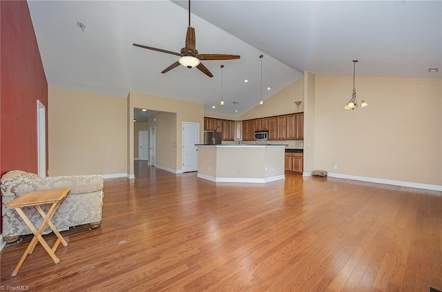 unfurnished living room with high vaulted ceiling, ceiling fan with notable chandelier, and light hardwood / wood-style floors