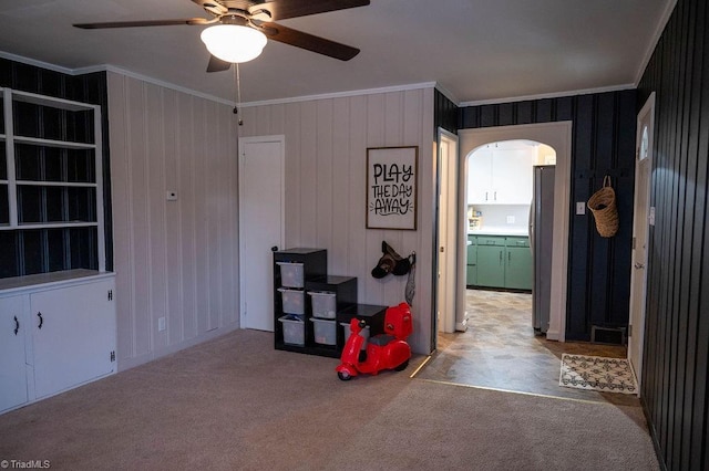 miscellaneous room featuring light carpet, ceiling fan, ornamental molding, and wood walls