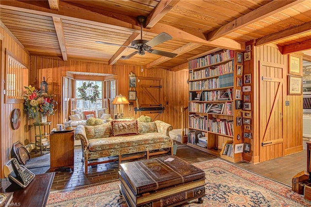 sitting room featuring ceiling fan, wood ceiling, wood walls, and beam ceiling