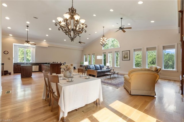 dining room with a towering ceiling, light hardwood / wood-style floors, ceiling fan with notable chandelier, and ornamental molding