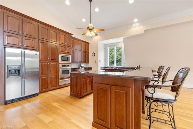 kitchen with a center island, ceiling fan, light wood-type flooring, appliances with stainless steel finishes, and a breakfast bar area