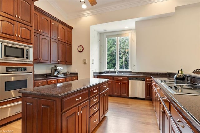 kitchen with appliances with stainless steel finishes, light wood-type flooring, dark stone counters, crown molding, and a kitchen island