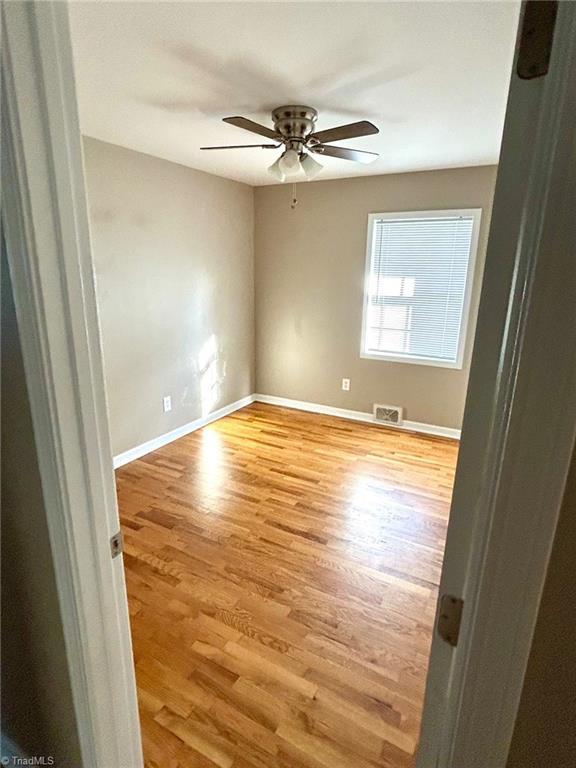 empty room with wood finished floors, baseboards, and a ceiling fan