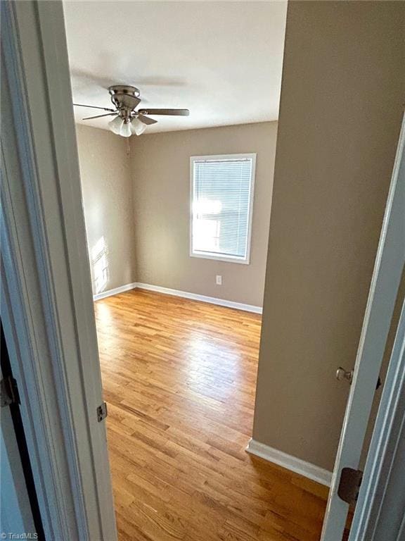 empty room featuring light wood finished floors, baseboards, and ceiling fan