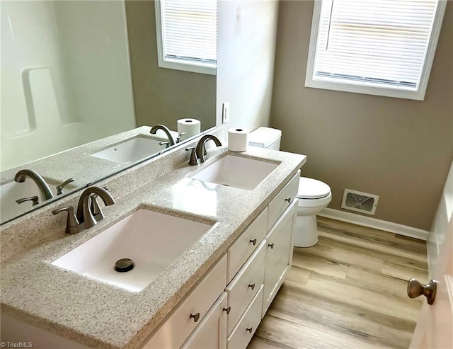 bathroom with toilet, healthy amount of natural light, wood finished floors, and baseboards