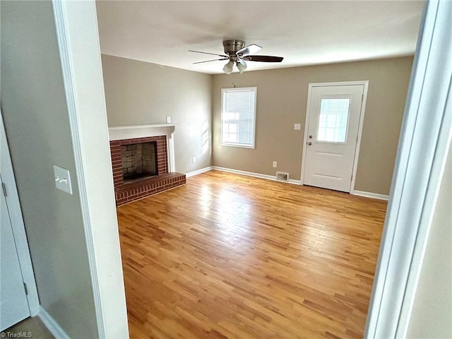 unfurnished living room with plenty of natural light, ceiling fan, light wood-style floors, and a brick fireplace