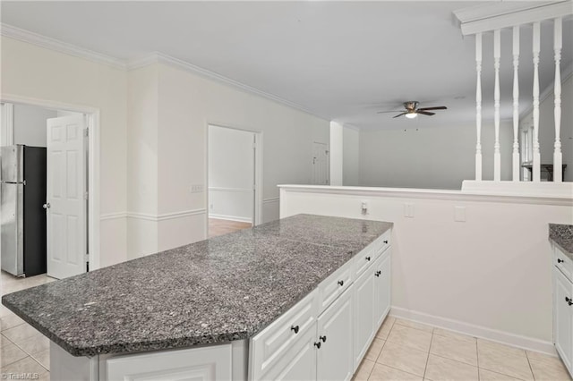 kitchen featuring light tile patterned flooring, stainless steel fridge, dark stone counters, white cabinets, and ornamental molding