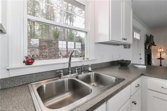 kitchen with a fireplace, crown molding, white cabinetry, and sink