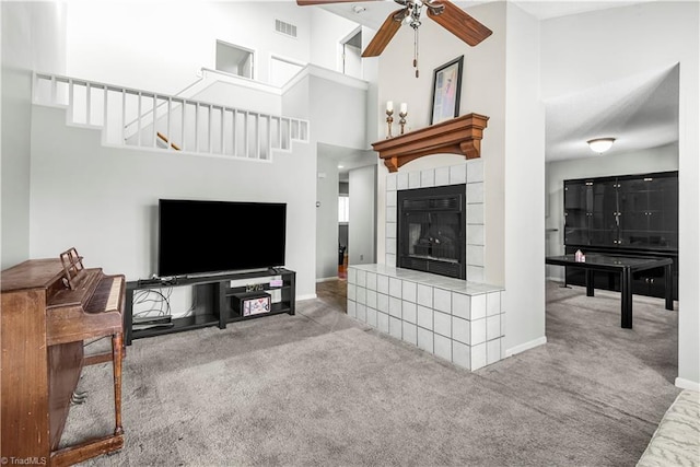 carpeted living room with ceiling fan, a tiled fireplace, and a high ceiling