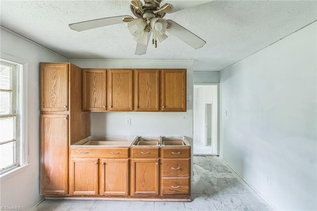 kitchen with brown cabinetry, a sink, a textured ceiling, and ceiling fan
