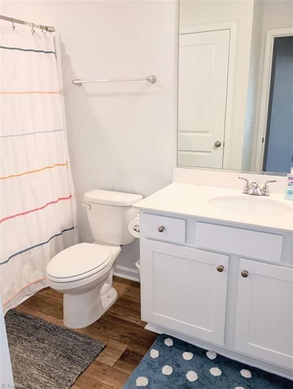 full bath featuring vanity, a shower with curtain, wood finished floors, baseboards, and toilet