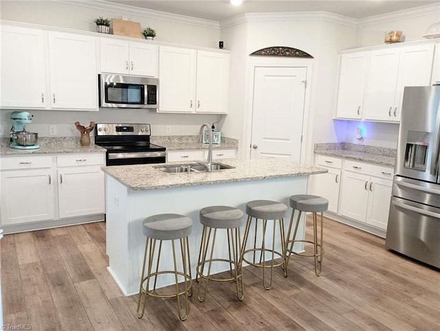 kitchen with ornamental molding, a center island with sink, light wood-style flooring, a sink, and stainless steel appliances