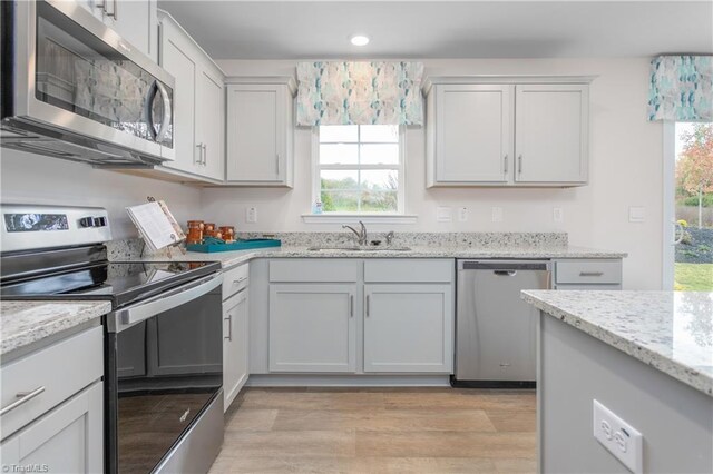 kitchen with light stone countertops, white cabinetry, sink, stainless steel appliances, and light wood-type flooring