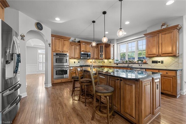 8501 Julina Dr, Oak Ridge, NC 27310 - kitchen with appliances with stainless steel finishes, brown cabinetry, dark wood-style flooring, an island with sink, and a sink