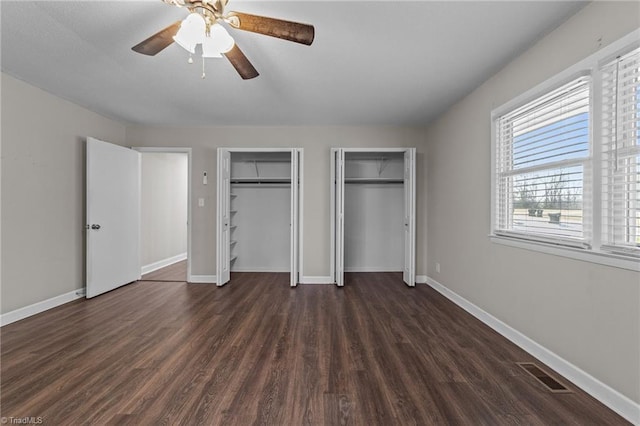 unfurnished bedroom featuring dark wood-type flooring, two closets, and ceiling fan