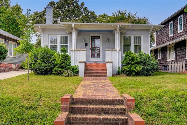 bungalow with a front yard, covered porch, brick siding, and a chimney