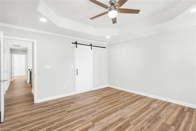 spare room with hardwood / wood-style floors, ceiling fan, a tray ceiling, and a barn door