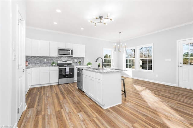 kitchen featuring decorative light fixtures, a kitchen island with sink, white cabinets, appliances with stainless steel finishes, and sink