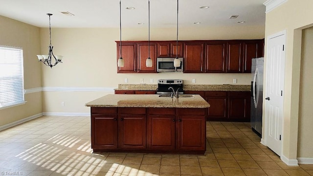 kitchen featuring light stone countertops, appliances with stainless steel finishes, decorative light fixtures, and an island with sink