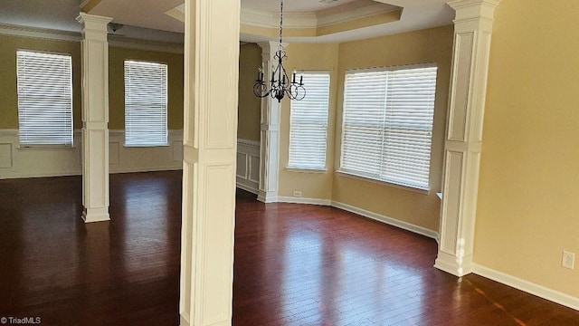 unfurnished dining area featuring dark wood-type flooring, an inviting chandelier, a raised ceiling, decorative columns, and crown molding