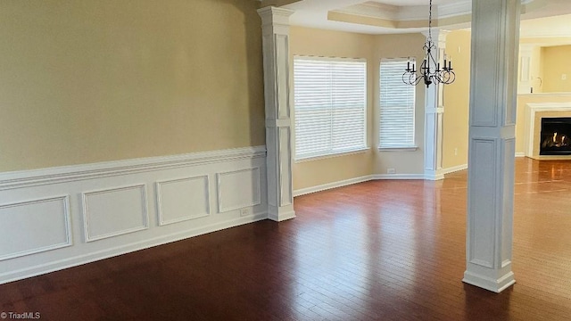 unfurnished dining area with a notable chandelier, decorative columns, crown molding, hardwood / wood-style floors, and a tray ceiling