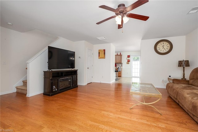 living area featuring visible vents, baseboards, ceiling fan, stairway, and light wood finished floors