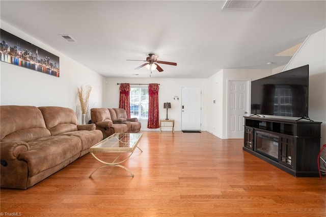 living room with ceiling fan, light wood finished floors, and visible vents
