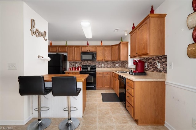 kitchen featuring a peninsula, backsplash, black appliances, and a breakfast bar