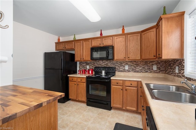 kitchen with brown cabinetry, decorative backsplash, a sink, and black appliances