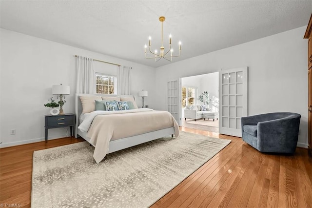 bedroom with an inviting chandelier, hardwood / wood-style flooring, baseboards, and a textured ceiling