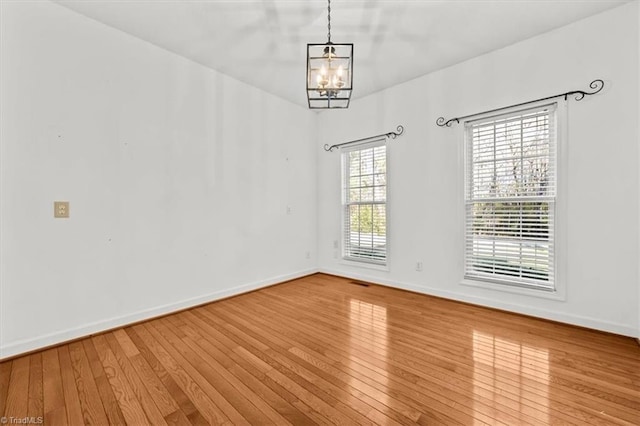 spare room featuring baseboards, a notable chandelier, and hardwood / wood-style flooring