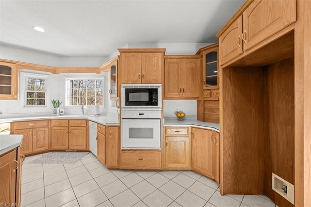 kitchen featuring light countertops, a sink, glass insert cabinets, light tile patterned floors, and white appliances