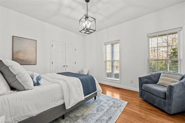bedroom with baseboards, visible vents, wood finished floors, and a chandelier