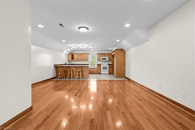 unfurnished living room featuring light wood-type flooring, lofted ceiling, baseboards, visible vents, and recessed lighting