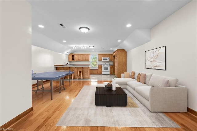 living room featuring vaulted ceiling, light wood-type flooring, baseboards, visible vents, and recessed lighting