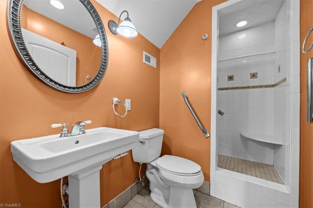 bathroom with toilet, tiled shower, a sink, tile patterned flooring, and visible vents