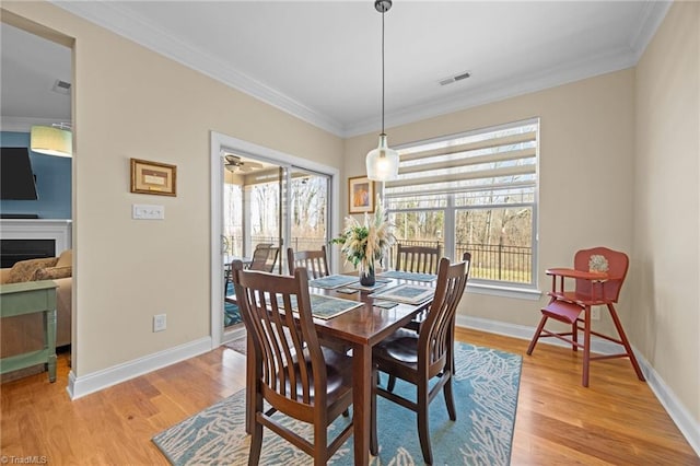 dining room featuring visible vents, crown molding, baseboards, light wood-style flooring, and a fireplace