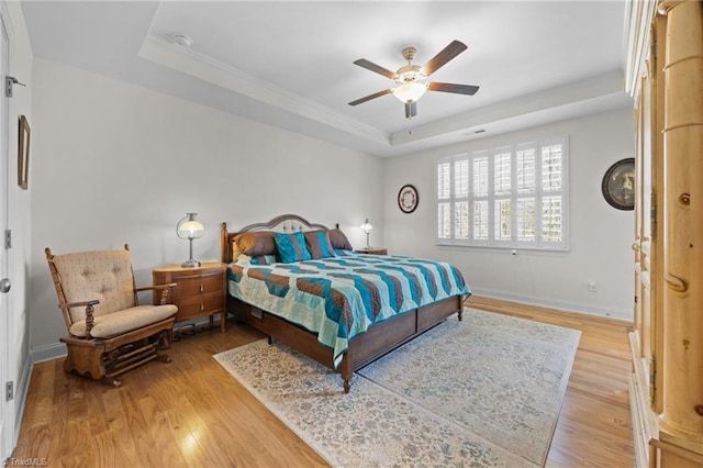 bedroom with baseboards, a raised ceiling, light wood-style flooring, and a ceiling fan