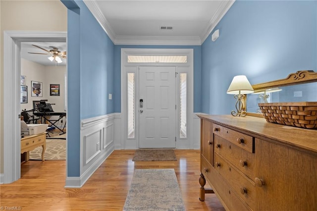 entryway featuring light wood finished floors, visible vents, ornamental molding, wainscoting, and a decorative wall